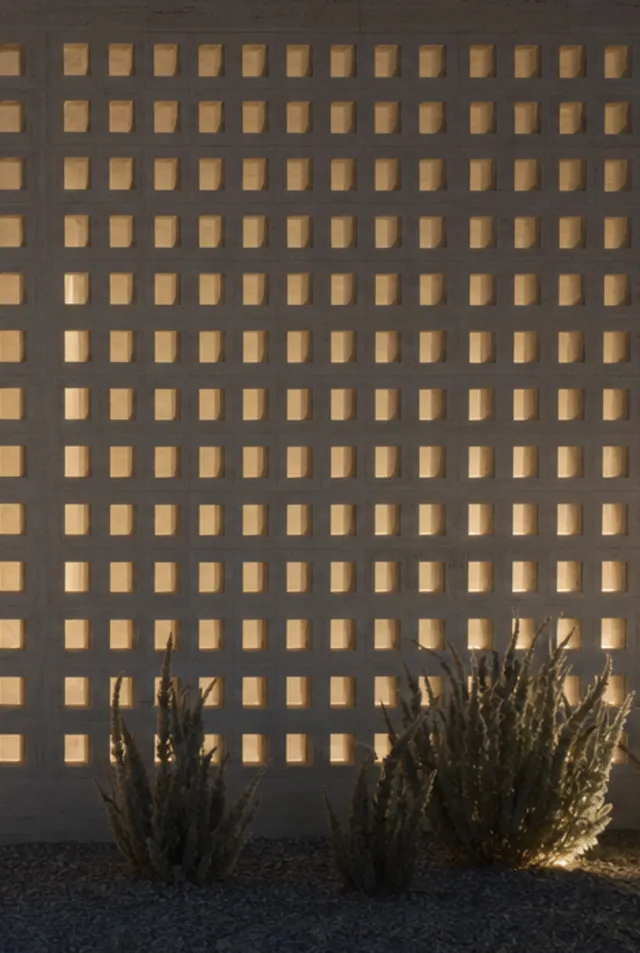 Detail of a travertine breeze-block screen at dusk, each cell glowing warm from the courtyard behind.