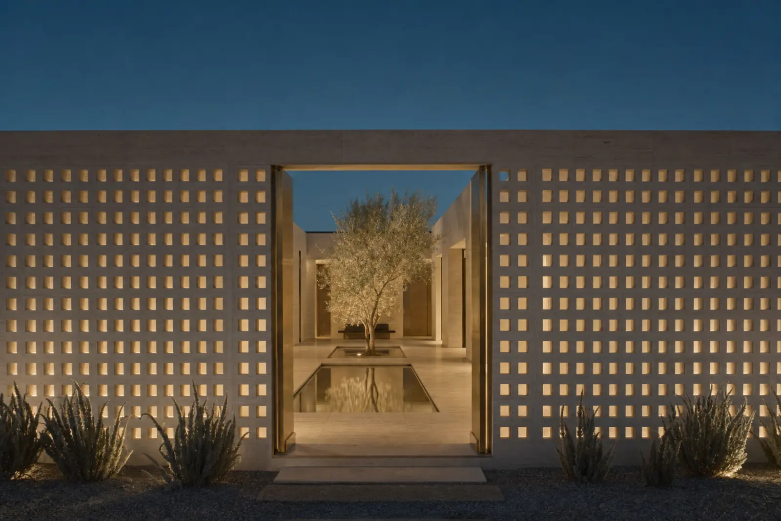 Lantern Court: a courtyard house seen through a travertine breeze-block screen at dusk, reflecting pool and olive tree within.