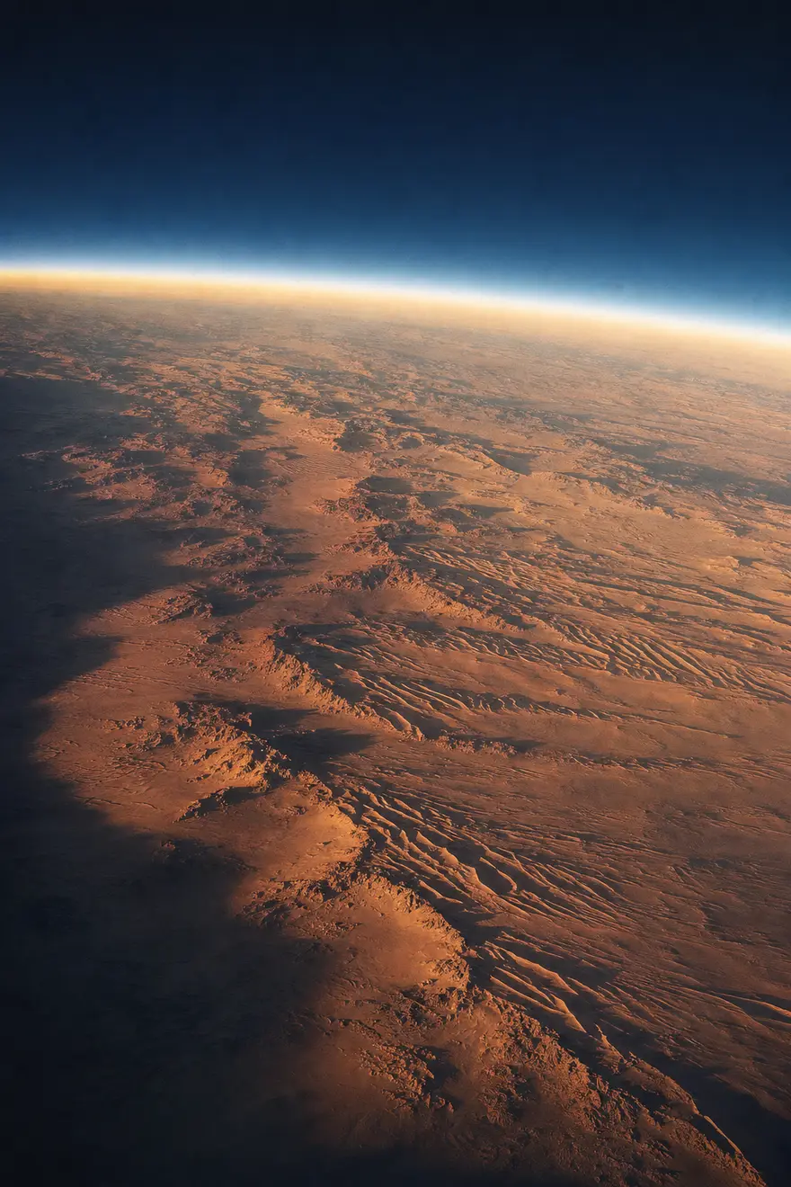 The Sahara from orbit at dawn: gold and ochre dune seas with long shadows under a thin glowing atmosphere